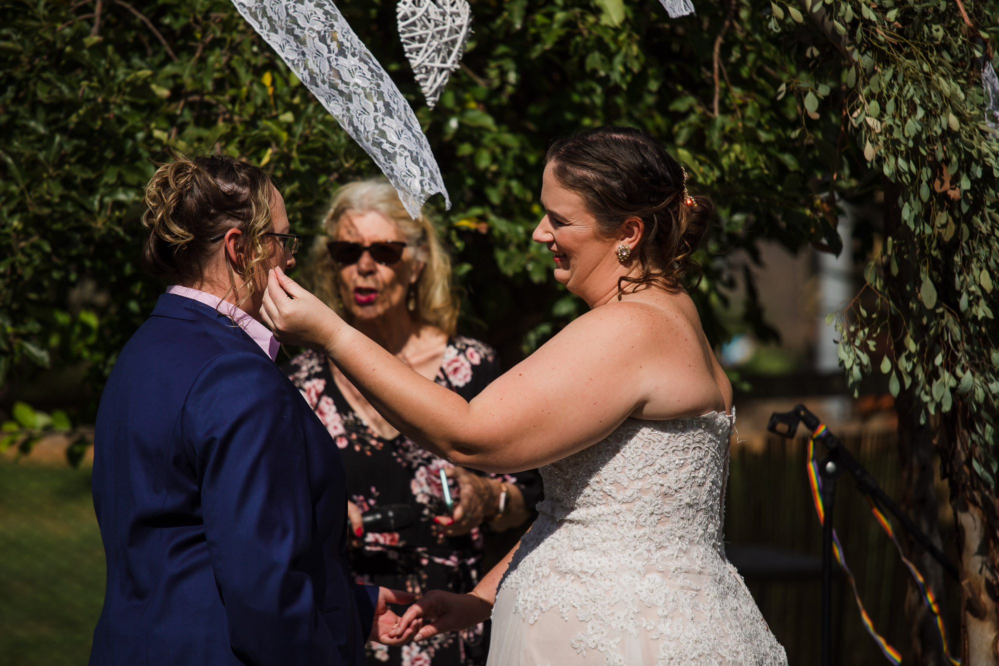 bride tucks a strand of hair behind the other brides ear during covid 19 wedding ceremony